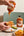 Sunnybank pineapple and habanero hot sauce being drizzled over a sandwich beside waffle fries.