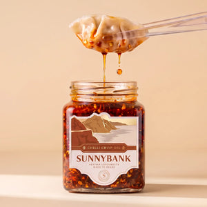 Dumpling held above a jar of Sunnybank chilli crisp oil, with chilli oil dripping from it.