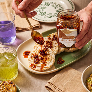Sunnybank chilli crisp oil spooned onto rice crackers from an open jar.