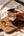 Hand holding a jar of Sunnybank chilli crisp oil over a wooden board beside a gold spoon.