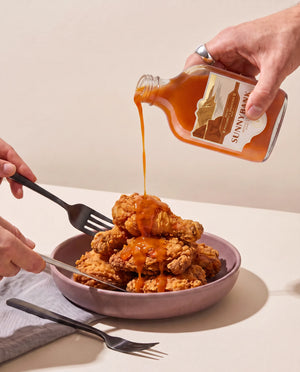 Sunnybank pineapple and habanero hot sauce being poured over a bowl of crispy fried chicken.