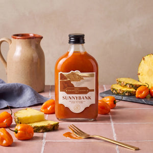 Bottle of Sunnybank smoky pineapple and habanero hot sauce with fresh chillies and pineapple slices.